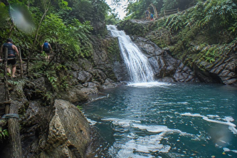 Waterfall sliding into a deep blue pool inside a forested gorge