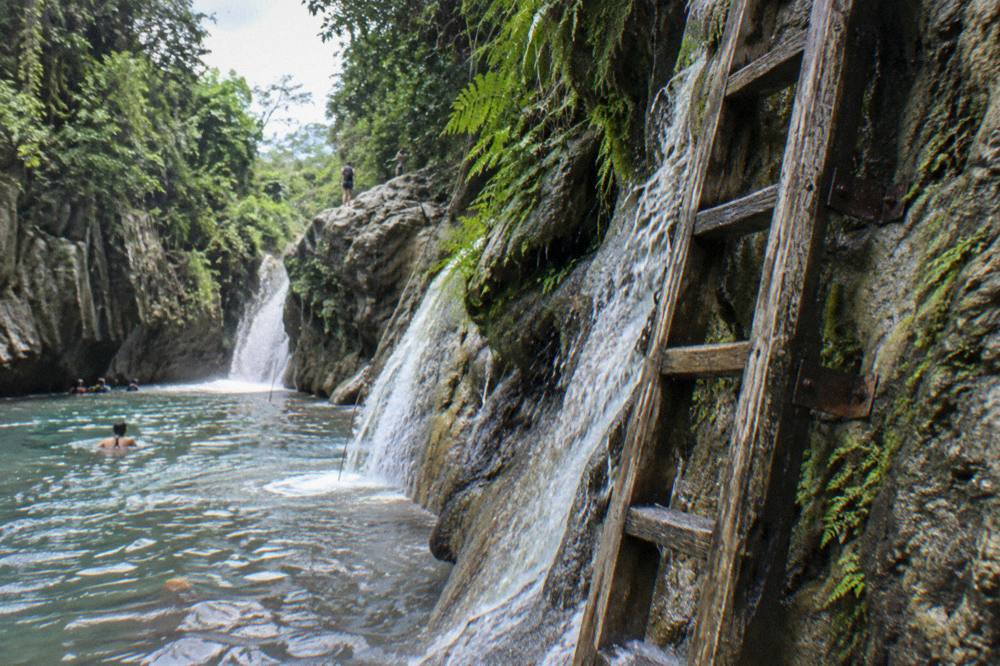 Wooden ladder bolted to a canyon wall beside a cascading waterfall